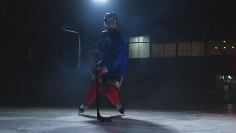 Male-hockey-player-with-a-puck-on-the-ice-arena-shows-dribbling-moving-directly-into-the-camera-and-looking-directly-into-the-camera-against-a-dark-background-in-the-smoke